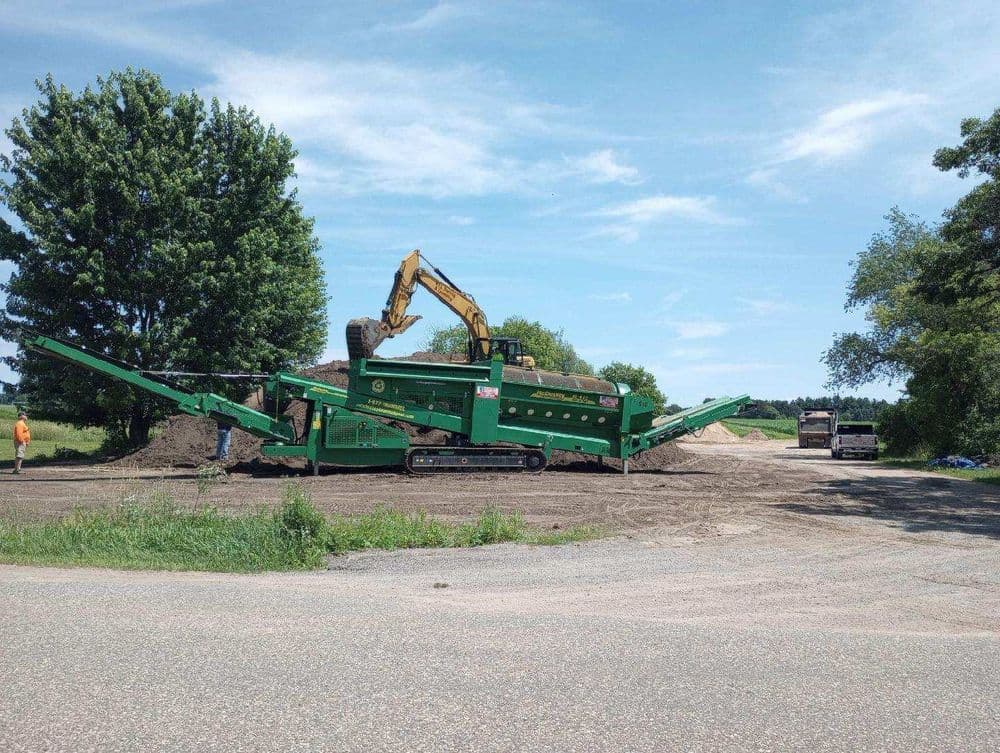 Heavy machinery on a construction site with excavator and soil processing equipment.