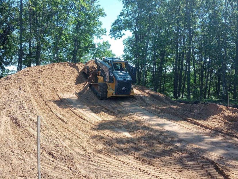 Skid steer loader moving dirt on a construction site amid lush trees.